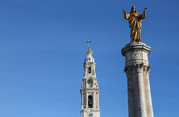 Golden statue of Jesus in the front and in the back the basilica of fatima with a clear blue sky