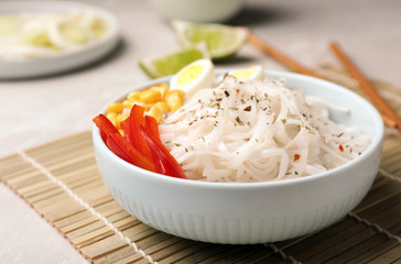 Bowl with rice noodles and vegetables on table