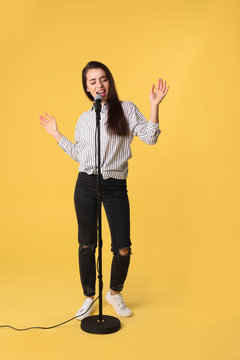 Young woman wearing casual clothes singing in microphone on color background