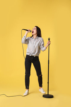 Young woman wearing casual clothes singing in microphone on color background