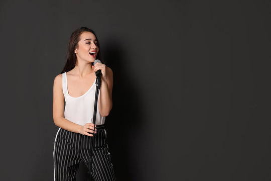 Young stylish woman singing in microphone on dark background. Space for text