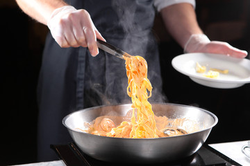 Cooking pasta with seafood. Chef's hands close-up, no face. Restaurant food.
