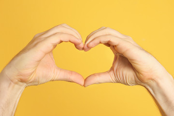 Man making heart with his hands on color background, closeup