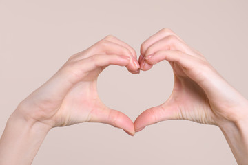 Young woman making heart with her hands on color background, closeup