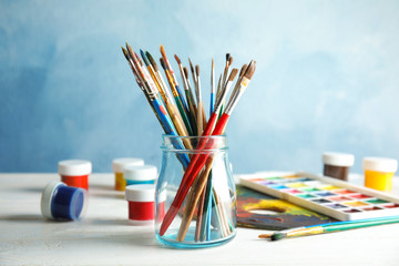Fototapeta premium Glass jar with brushes and paints on table against color background