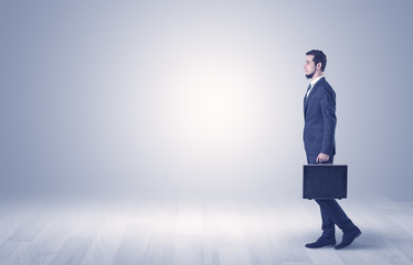Fototapeta premium Successful businessman walking in front of an empty wall with briefcase on his hand 