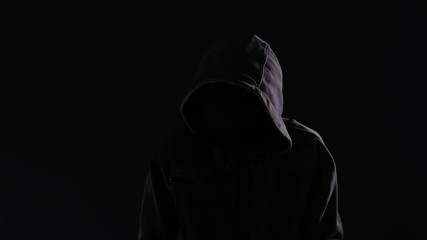 Hooligan with hoodie and obscured face walking the city streets at night, looking spooky and threatening