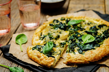 Spinach Ricotta Galette with fresh spinach leaves on a wood background