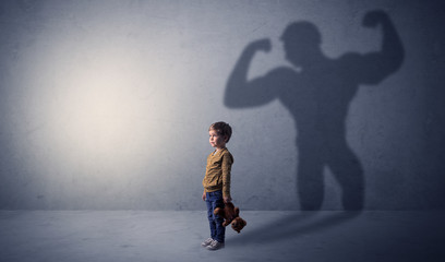 Little waggish boy in an empty room with musclemen shadow behind
