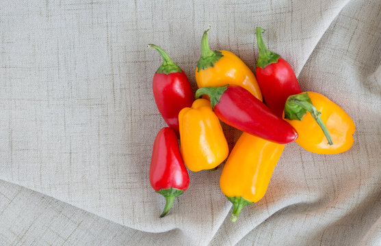 a group of bright red and orange mini sweet peppers on a tan linen cloth with copy space
