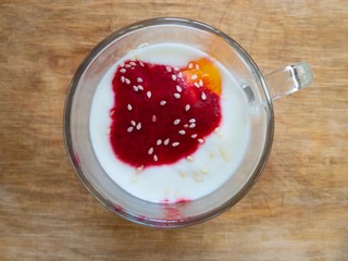 Top view on a glass of yogurt topped with honey, raspberries mash and sesame seed