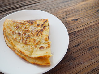 Traditional french crepe (or pancake) on a white plate, with sugar on top (called crêpe Suzette), dark brown wood background