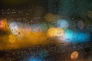 Raindrops on window glass close up blurred bokeh night lights on background