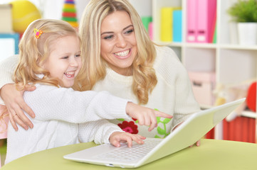 mother with little daughter using modern laptop