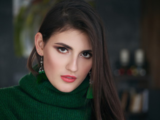 Obraz premium Casual close up portrait of happy young brunette woman with trendy makeup green sweater and custom brush earrings.