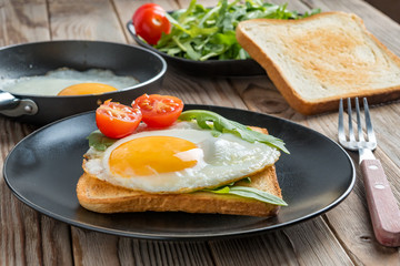 Clouse up view of fried eggs on black plate and pan with fork, mushrooms and rukkola. Soft focus