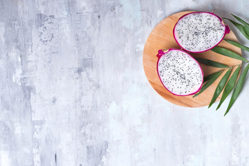 Pitaya or Dragon Fruit with palm leaf on wooden round plate on gray stone background with copy space, flat lay