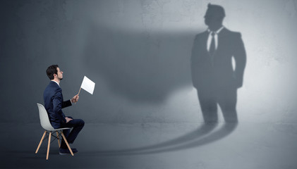 Humble businessman staying and offering stuffs to a huge angry bull shadow
