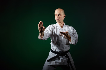 Active athlete trains formal karate exercises on a dark green background © andreyfire