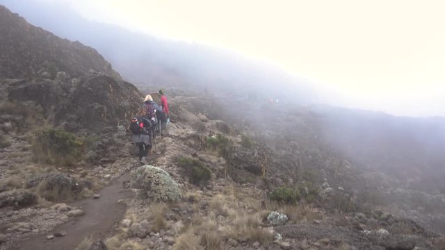 Pan Shot of Two Hikers and a Guide on Mount Kilimanjaro Walking trough Misty Clouds with other Hikers in Backgorund