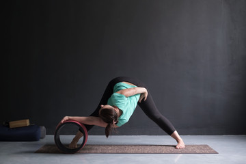 Woman doing yoga asana Wide Legged Forward Bend using special wheel.