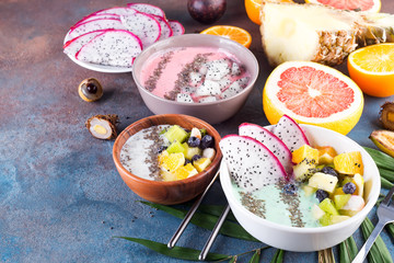 breakfast green yoghurt bowl topped with pitaya, pineapple, chia seeds and berries with palm leaf on stone background, top view