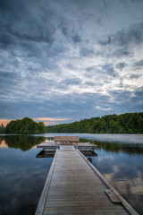 Wooden foot bridge leading out to a platform with a bench on a calm lake in Sweden