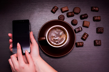 a cup of coffee, chocolate candy and a phone on a dark background.