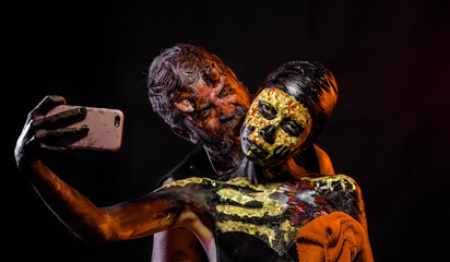 Halloween man satan and woman skeleton pose for smartphone