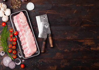 Plastic tray with raw pork ribs and vintage hatchets on wooden background. Fresh tomatoes and red...