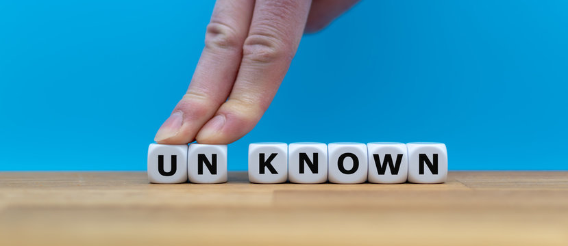 Dice form the word "UNKNOWN" while two fingers push the letters "UN" away in order to change the word to "KNOWN".
