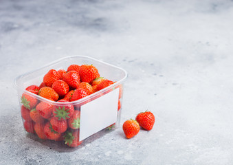 Plastic tray container of fresh organic healthy strawberries on stone kitchen table background....