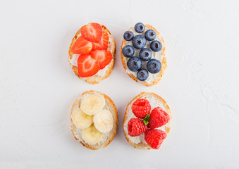 Fresh healthy mini sandwiches with cream cheese, fruits and berries. Strawberries, blueberries, bananas and raspberries on stone kitchen table background.Top view