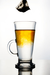 Brewing of hot beverage with tea bag in glass cup on white background