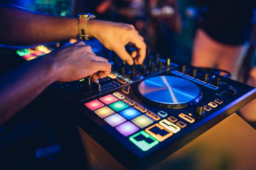 DJ plays live set and mixing music on turntable console at stage in the night club. Disc Jokey...