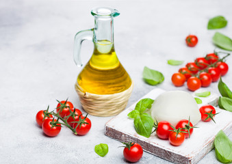 Fresh Mozzarella cheese on vintage chopping board with tomatoes and basil leaf with olive oil on stone kitchen table background.
