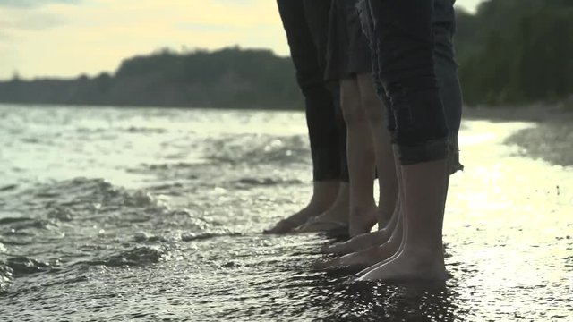 Three people's legs in the water against crashing waves.