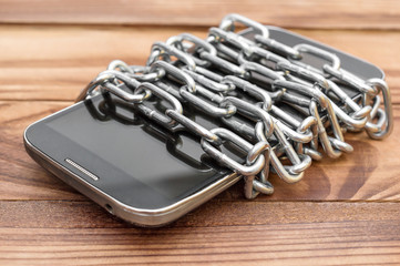 Smartphone wrapped by chain on the wooden table.