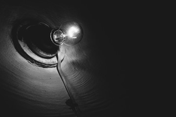 Incandescent lamp burns inside dark room close-up. Illumination. Old light bulb on rough wall. Lamp illuminate basement in grayscale. Light in darkness. Minimalist monochrome background. Copy space.