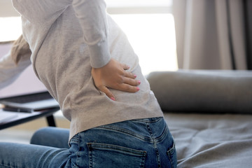 Rear close up view at woman touching aching back feeling lower lumbar muscular kidney pain rubbing tensed muscles suffering from backache sitting in sedentary incorrect posture, backpain concept - obrazy, fototapety, plakaty