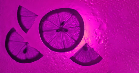Fototapeta na wymiar lemon wedges on pink purple water drop background