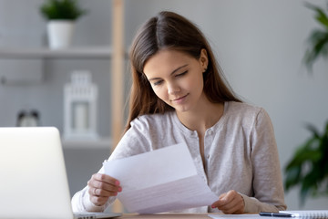 Smiling young woman doing paperwork holding letter of advice bill reading paper checking post mail...