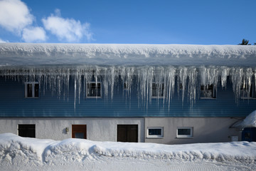 icicle at roof of house in winter with blue sky and snow