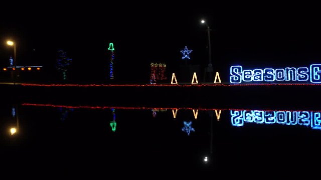4K Seasons Greetings Neon Sign On Water With Water Ripples And Neon Christmas Trees Pan Right To Left