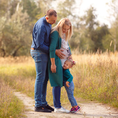 Fototapeta premium Portrait of pretty young pregnant woman with her young husband and cute little baby walking in park in sunny day. Family. Maternity. Happiness. Health.