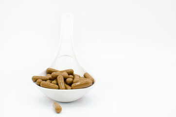 Plastic spoon full of brown capsule pills, as a concept of health issues. Isolated on a white background 
