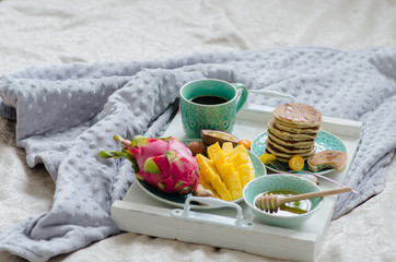 Breakfast in bed with tropical fruits, pancakes and coffee on a tray.