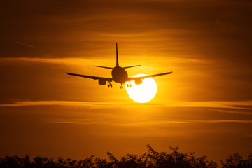 Fototapeta na wymiar Silhouette of an air plane over the sun with beautiful red clouds in background
