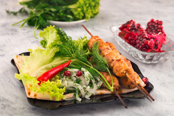 Kebab on wooden skewers. Fresh lettuce. Dill and hot pepper. Pomegranate seeds. Light background.
