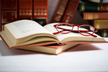 Stack of books with red glasses placed on the open book in library.